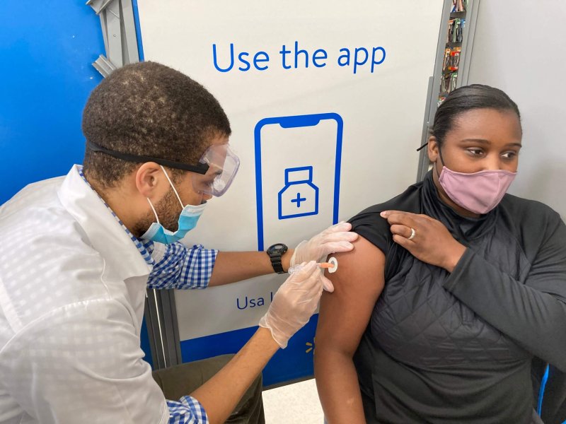 Walmart store manager Essica Clifton looks away as Ashton Cheatham, pharmacy manager, gives her a shot of covid-19 vaccine. Credit: Pine Bluff Commercial/Byron Tate