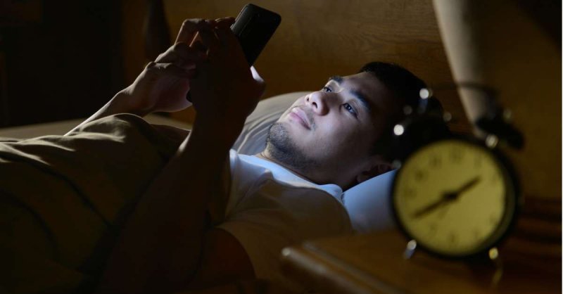 young man using a smartphone in his bed at night picture id